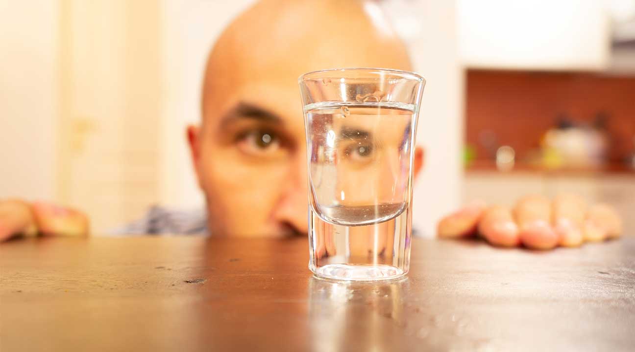 alcohol addiction man staring at a shot glass on a table