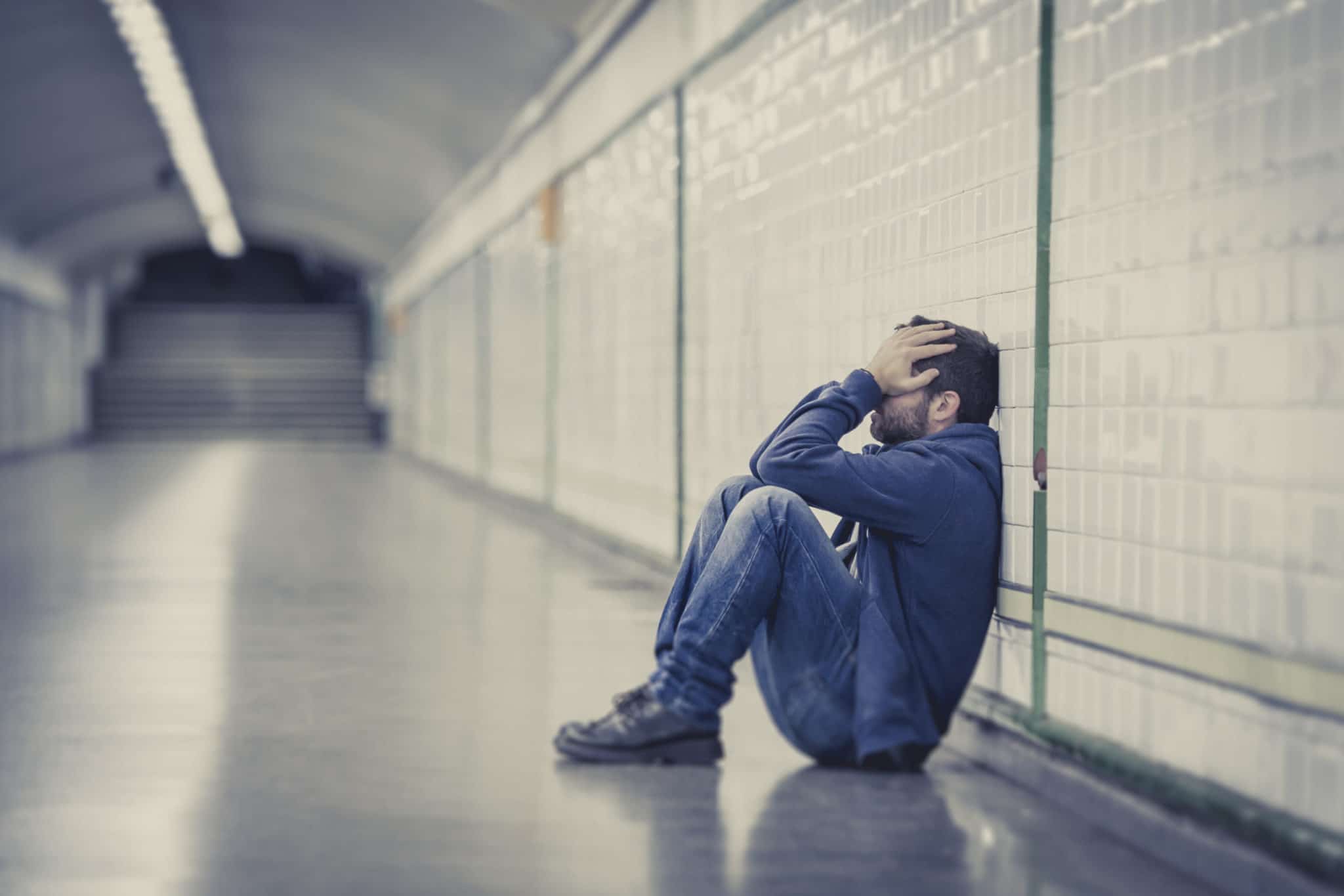 sad man sitting on the ground at a train station