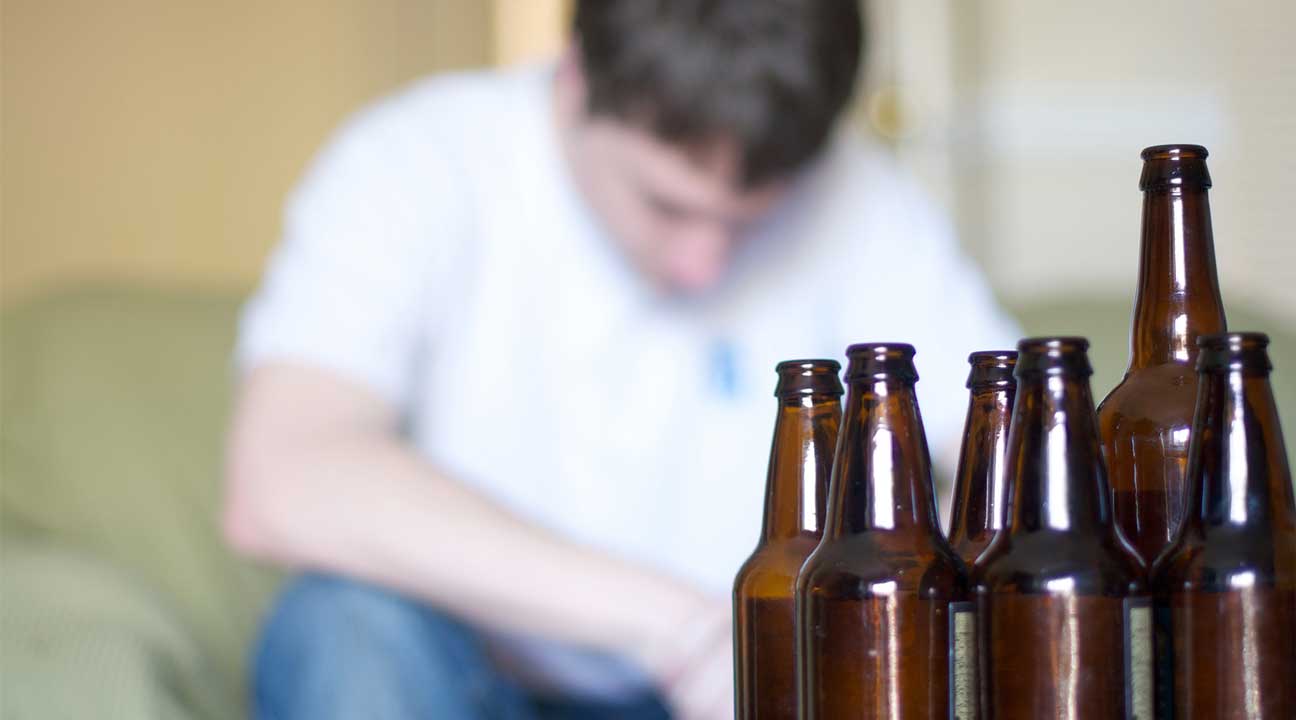 man drinking too much surrounded by empty bottles