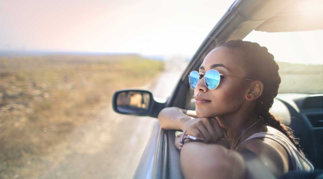 young woman wearing glasses looking out of a car window on a sunny day