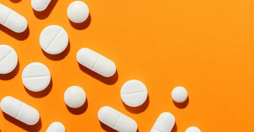 Assorted white medicinal pills on an orange background