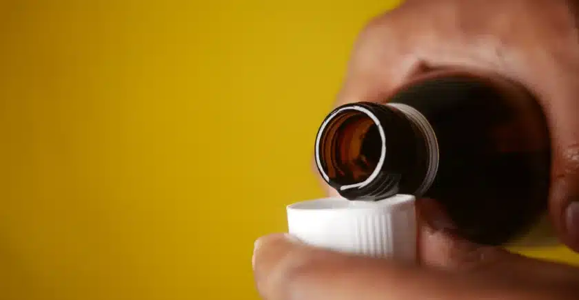 Pouring a dose of cough syrup into a cap, with a yellow background