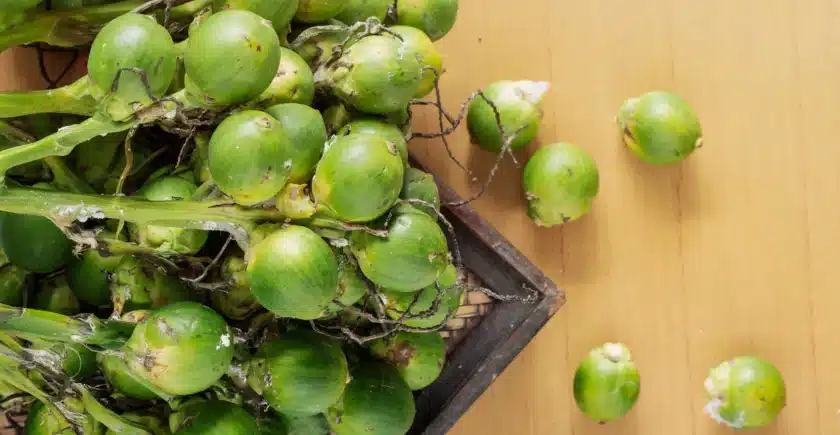 Top view of a bunch of green betel nuts on a wooden surface, with some loose betel nuts scattered around.