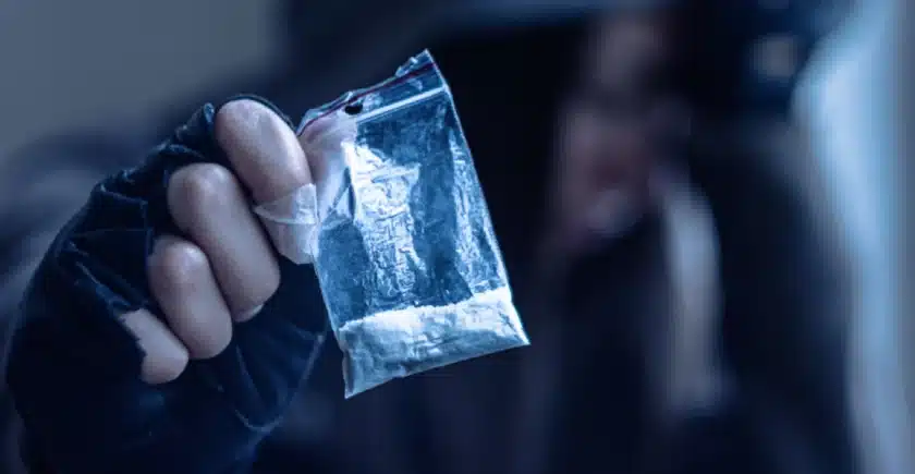Man in black hoodie holding a dime bag of a white powder substance.